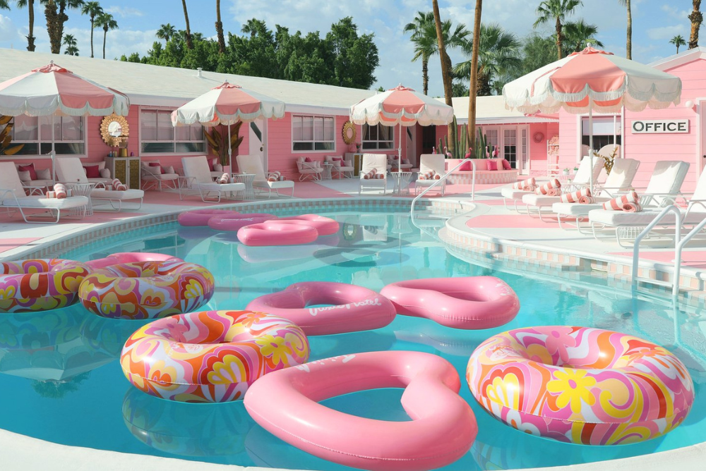 Trixe Motel in Palm Springs. Pastel coloured inflatable rings float on a kidney bean-shaped pool, surrounded by light pink bungalows with white sun loungers.